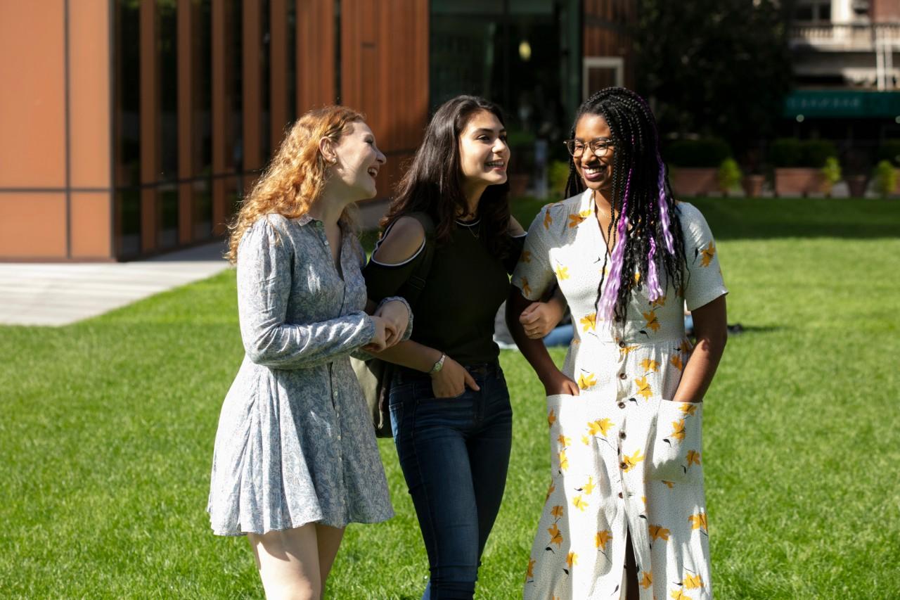 3 young women, arm in arm, crossing campus